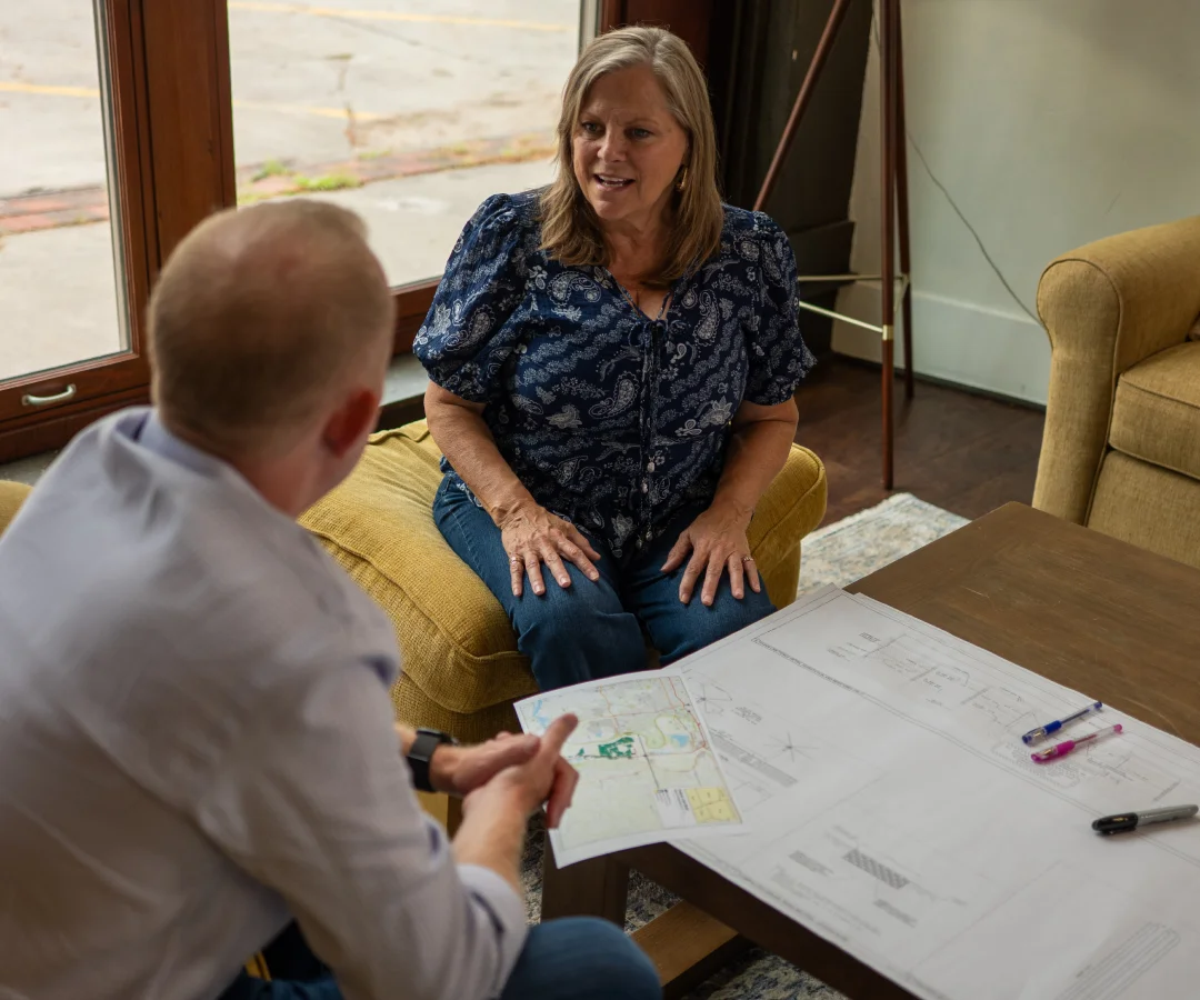 Two people discuss project plans and maps at a table in a local community setting