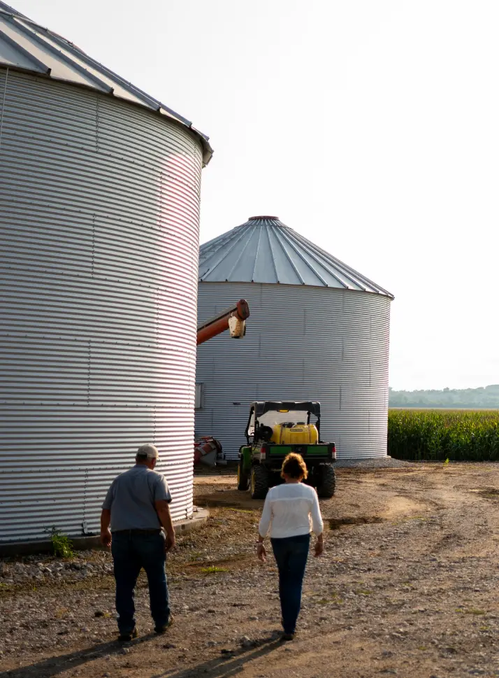 Two farmers walking past grain bins alongside a cornfield